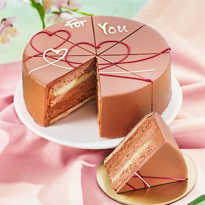 Petite tarte &agrave; la ganache au chocolat au lait, d&eacute;cor&eacute;e de c&oelig;urs en gla&ccedil;age et de l&rsquo;inscription &laquo; For You &raquo;. Plusieurs couches de cr&egrave;me et de biscuit sont visibles ; une part est servie sur une petite assiette.