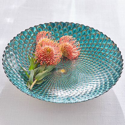 Dekorative Glasschale in T&uuml;rkis mit strukturierter Oberfl&auml;che, gef&uuml;llt mit zwei rosafarbenen Bl&uuml;ten als stilvolles Tischobjekt.