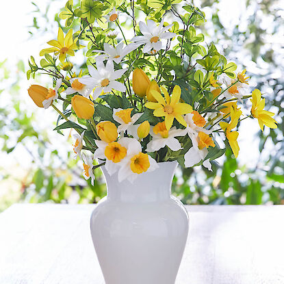 Fr&uuml;hlingsstrau&szlig; mit Narzissen und Margeriten in Gelb und Wei&szlig;, arrangiert in wei&szlig;er Vase vor Fensterlicht.