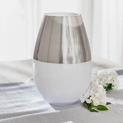 Moderne Vase in Wei&szlig; mit silberfarbenem Akzent, minimalistisch inszeniert auf hellem Stoff mit wei&szlig;en Bl&uuml;ten.