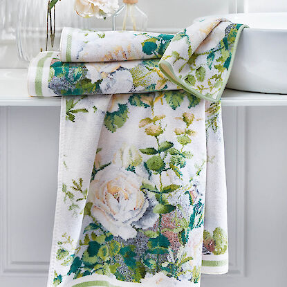 Florale Handt&uuml;cher mit Rosenmotiv in Gr&uuml;n- und Cremet&ouml;nen, dekorativ drapiert im hellen Badezimmer.
