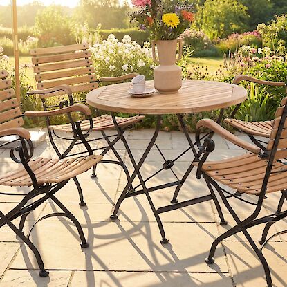 Gartenm&ouml;bel-Set aus Holz und Metall mit rundem Tisch und vier St&uuml;hlen, arrangiert auf sonniger Terrasse im Garten.