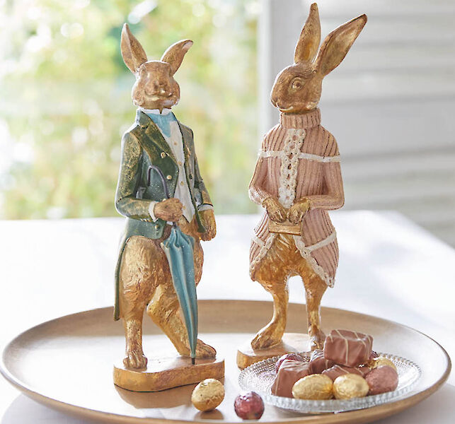 Dekorative Hasenfiguren im Vintage-Stil, als Paar auf Tablett arrangiert, erg&auml;nzt mit kleinen Schokoladenpralinen.