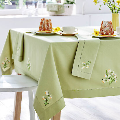 Table dress&eacute;e au printemps avec nappe verte et serviettes brod&eacute;es de fleurs, g&acirc;teaux et service &agrave; caf&eacute;