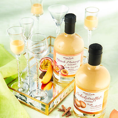 Deux bouteilles de liqueur aux &oelig;ufs p&ecirc;che&ndash;fruit de la passion et truffe chocolat, avec verres et fruits sur un plateau