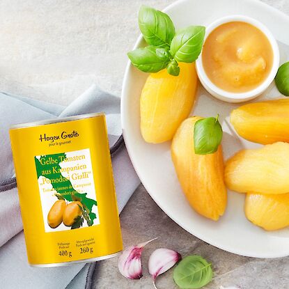 Dose &bdquo;Gelbe Tomaten aus Kampanien &ndash; Pomodori Gialli&ldquo; von Hagen Grote neben gesch&auml;lten gelben Tomaten mit Basilikum auf einem Teller