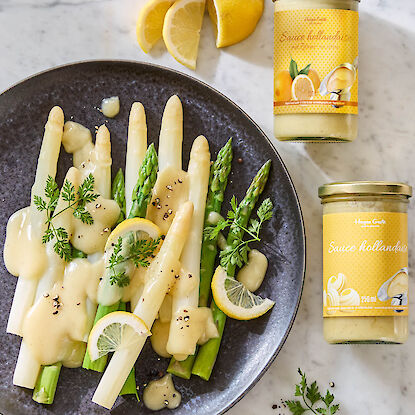Wei&szlig;er und gr&uuml;ner Spargel mit Sauce hollandaise auf Teller, daneben Gl&auml;ser mit Sauce hollandaise