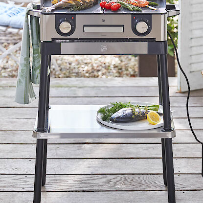 Elektrischer Standgrill mit Fisch, Garnelen, Spargel und Tomaten auf Grillrost auf Terrasse