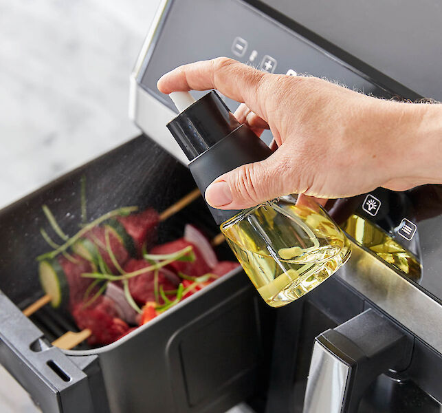 Hand spr&uuml;ht &Ouml;l auf Fleisch und Gem&uuml;se in Hei&szlig;luftfritteuse