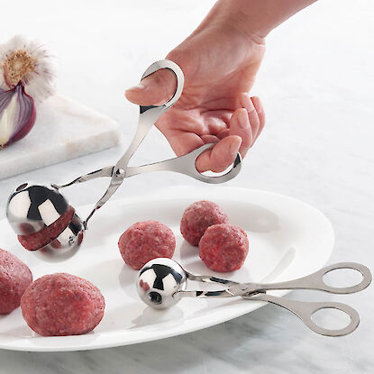 Zange zum Formen von Fleischb&auml;llchen aus Hackfleisch auf Teller