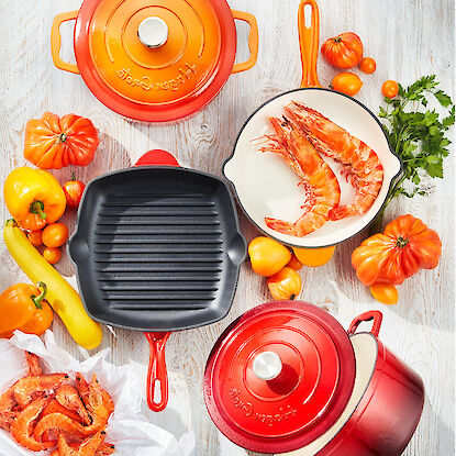 Gusseisen Kochgeschirr Set mit Grillpfanne, Topf und Garnelen auf hellem Tisch