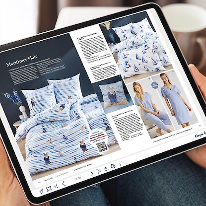 Person h&auml;lt Tablet mit digitalem Bl&auml;tterkatalog, zeigt Bettw&auml;sche und Nachtw&auml;sche im maritimen Design