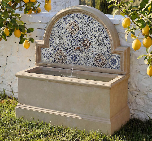 Gartenbrunnen aus Stein mit blau-wei&szlig;em Fliesenmuster, umgeben von Zitronenb&auml;umen im mediterranen Garten