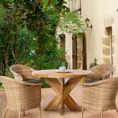Runder Gartentisch aus Holz mit vier Rattanst&uuml;hlen auf Terrasse, umgeben von gr&uuml;ner Gartenlandschaft