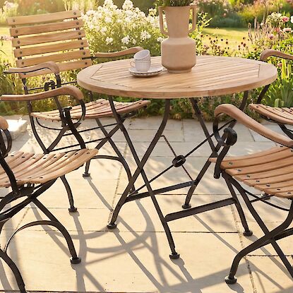 Gartensitzgruppe aus Holz mit rundem Tisch und St&uuml;hlen auf sonniger Terrasse im bl&uuml;henden Garten