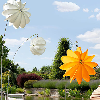 Dekorative Windspiele in Bl&uuml;tenform aus Stoff in Wei&szlig; und Gelb im Garten am Teich aufgeh&auml;ngt