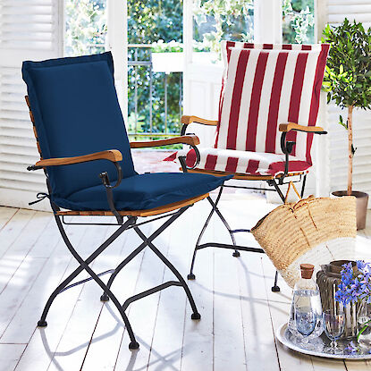 Klappst&uuml;hle mit Polstern in Blau und Rot gestreift auf heller Veranda mit Blick ins Gr&uuml;ne