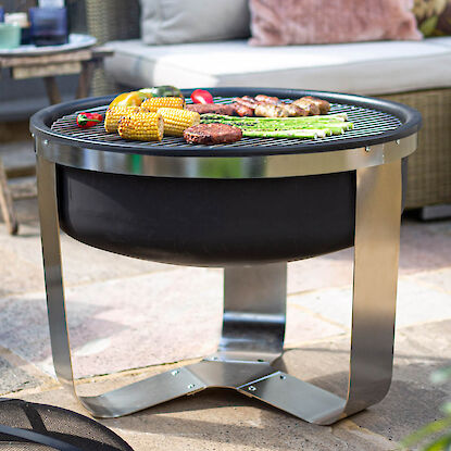 Runde Feuerstelle mit Grillrost aus Metall, belegt mit Gem&uuml;se und Fleisch auf Terrasse im Garten