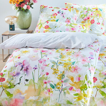 Bettw&auml;sche mit farbenfrohem Blumenmuster in Aquarelloptik, dekorativ auf einem Bett arrangiert