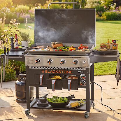 Gasgrill mit Grillplatte im Garten, belegt mit Fleisch, Gem&uuml;se und Spiegeleiern, ausgestattet mit Ablagen und Zubeh&ouml;r