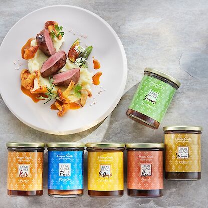 Hagen Grote Demi-Glace Saucen im Glas mit Rind, Kalb, Fisch, Gefl&uuml;gel und Gem&uuml;se neben Teller mit Fleischgericht