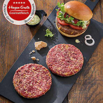Frische Burger-Patties aus Rindfleisch und fertiger Burger mit Salat, Tomate und Sauce, pr&auml;sentiert auf Schneidebrett