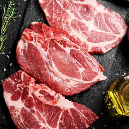 Rohe Nackensteaks mit Marmorierung auf Schneidebrett, mit &Ouml;l, Knoblauch und Kr&auml;utern angerichtet