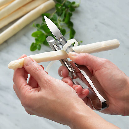 Spargelsch&auml;ler in Anwendung, H&auml;nde sch&auml;len wei&szlig;en Spargel pr&auml;zise und d&uuml;nn f&uuml;r die Zubereitung