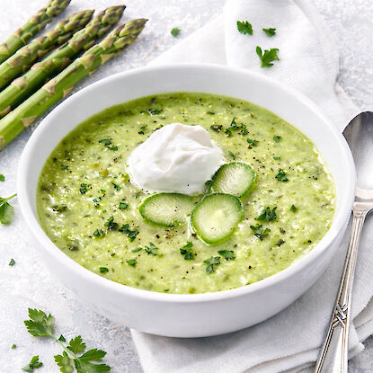 Cremige gr&uuml;ne Spargelsuppe mit Sahnehaube und Kr&auml;utern, serviert in Schale, frischer Spargel daneben