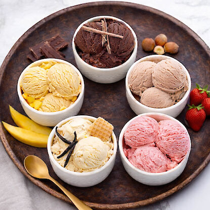 Verschiedene Eissorten in Schalen mit Schokolade, Vanille, Erdbeere und N&uuml;ssen, angerichtet auf Servierplatte