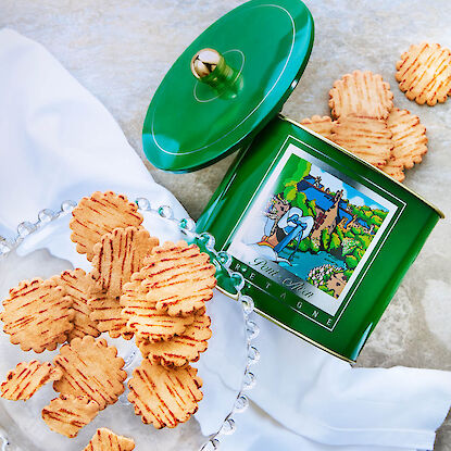 Knusprige Butterkekse neben gr&uuml;ner Geb&auml;ckdose, dekorativ serviert auf Glasplatte