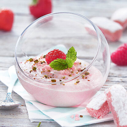 Cremiges Himbeer-Dessert im Glas mit Minze und gehackten Pistazien, dekorativ angerichtet