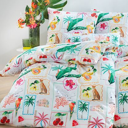 Bettw&auml;sche mit tropischem Muster aus Palmen, Fr&uuml;chten und Tieren in bunten Farben, dekorativ arrangiert im Schlafzimmer