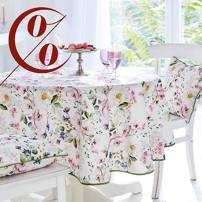 Runde Tischdecke mit floralem Muster und passenden Kissen, gedeckter Tisch mit Gl&auml;sern und Geb&auml;ck, Rabattaktion hervorgehoben