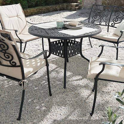 Gartenm&ouml;bel-Set aus Metall mit rundem Tisch und gepolsterten St&uuml;hlen auf Terrasse im Gr&uuml;nen