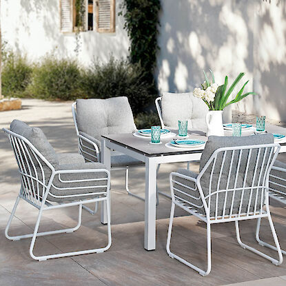 Modernes Gartenm&ouml;bel-Set mit Tisch und gepolsterten St&uuml;hlen auf sonniger Terrasse, gedeckt mit Geschirr und Gl&auml;sern