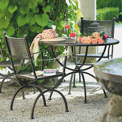 Gartenm&ouml;bel-Set aus Metall mit rundem Tisch und St&uuml;hlen, dekoriert mit Rosen und Getr&auml;nken im gr&uuml;nen Garten