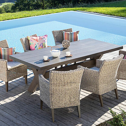Gro&szlig;es Gartenm&ouml;bel-Set mit Esstisch und Geflechtst&uuml;hlen auf Holzterrasse am Pool, dekoriert mit Kissen und Geschirr