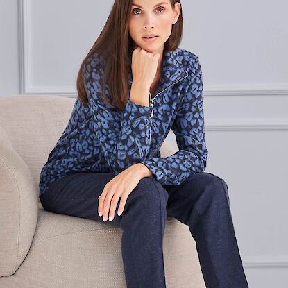 Damenoutfit mit gemustertem Oberteil und dunkler Hose, sitzend auf Sessel im Studio, moderner Look