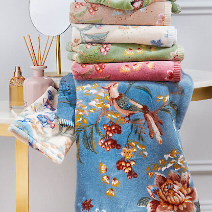 Stapel Handt&uuml;cher mit floralem Muster und Vogelmotiv in verschiedenen Farben, dekorativ im Badezimmer arrangiert