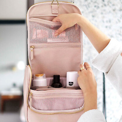 H&auml;ngende Kosmetiktasche in Rosa mit Rei&szlig;verschlussf&auml;chern, gef&uuml;llt mit Pflegeprodukten im Badezimmer