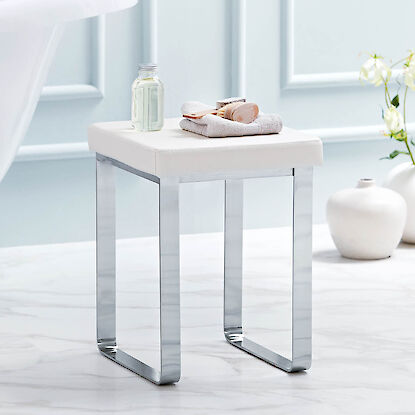 Badezimmerhocker mit gepolsterter Sitzfl&auml;che und Metallgestell, dekoriert mit Handtuch und Pflegeprodukten