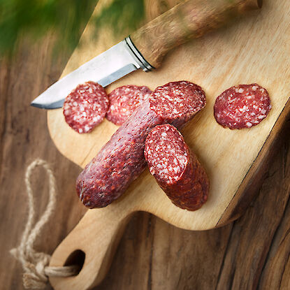 Salami tranchée sur une planche en bois avec un couteau.