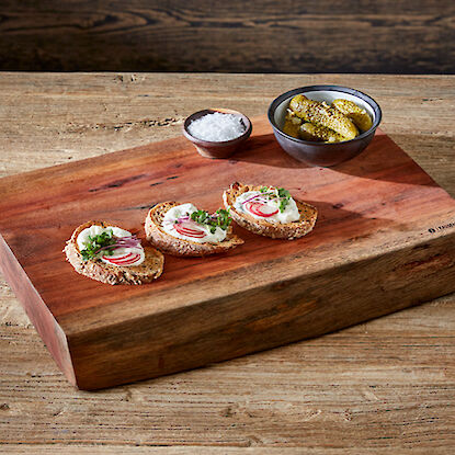 Trois tranches de pain garnies sur une planche en bois avec du sel et des cornichons dans des bols.