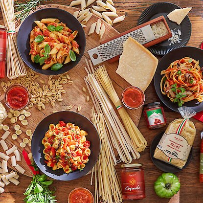 Différents plats de pâtes avec sauce tomate, fromage et ingrédients frais sur une table en bois.