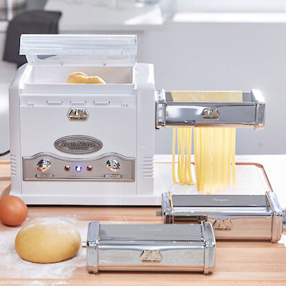 Machine à pâtes avec accessoires, étalant de la pâte fraîche sur une planche en bois, prête à être coupée en tagliatelles.