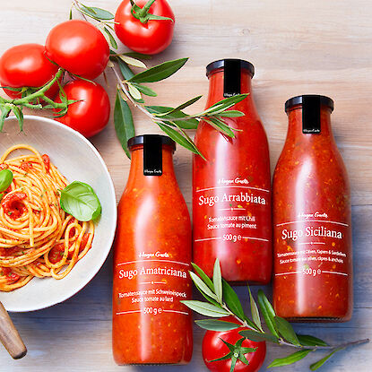 Trois bouteilles de sauces tomate italiennes avec des tomates fraîches et des feuilles d'olivier.