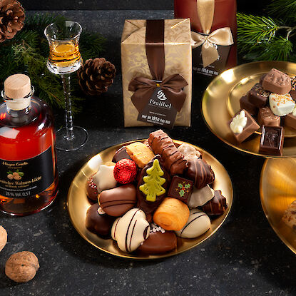 Délices festifs : pralines, chocolat, stollen, accompagnés de liqueur de noix et de champagne, entourés de branches de sapin.