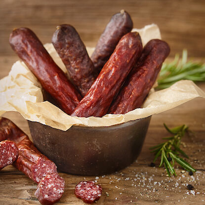 Saucisses sèches disposées dans un bol en métal sur une table en bois.