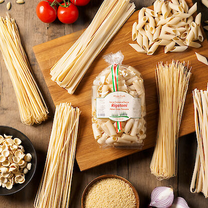 Pâtes italiennes variées sur une table en bois avec basilic, tomates, et ail.